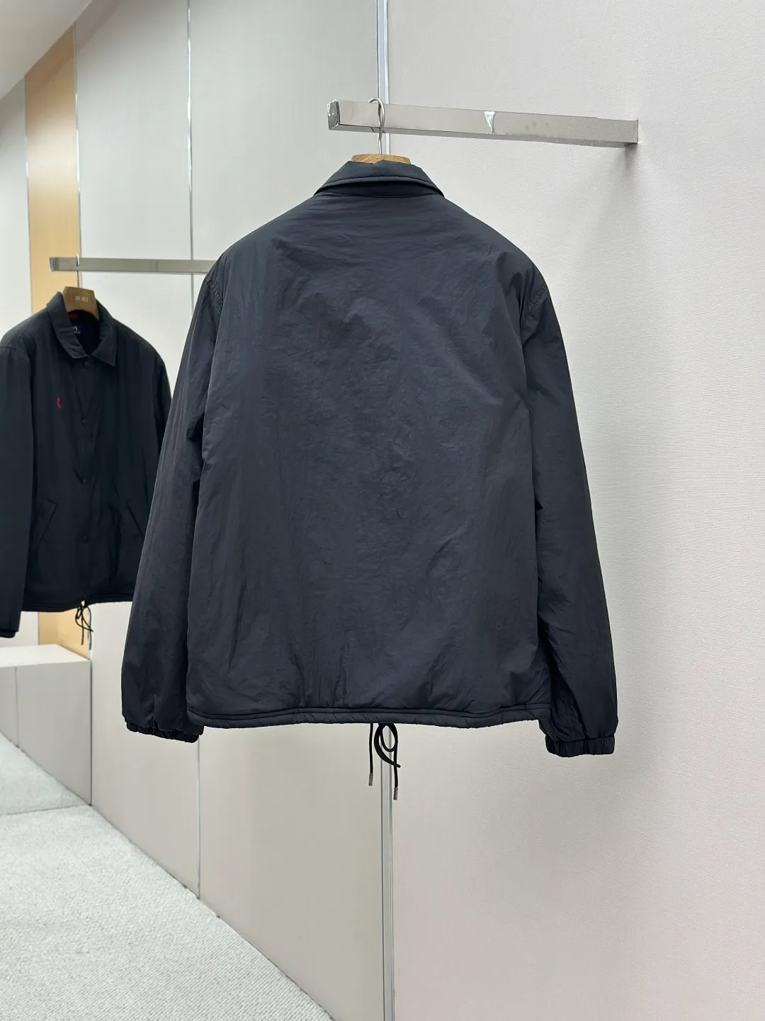 P650 RAH LAUREN RL red label lapel is light and thin. It is made of high-density nylon taffeta with a density of about 210T-300T. The surface is smooth and slightly matte. It has excellent windproof and waterproof performance (with R water-repellent treatment). It has strong wrinkle resistance and is easy to care for. It adopts the vat dyeing process (the dye penetrates into the fiber) and the color fastness reaches ISO level 4 or above to avoid fading or color transfer after washing. The lightweight cotton-polyester blend lining (65% Polyester + 35% Cotton) reduces the friction between the fabric and inner clothing and improves the smoothness of wearing. The blended material combines breathability and durability to avoid the stuffy feeling of pure nylon lining. The classic coach (Jaet) loose fit has a slightly dropped shoulder line (the shoulder width is 1-2cm wider than the standard fit), the length reaches the hips, and the sleeves are slightly tapered straight sleeves, taking into account freedom of movement and casual style. Flat satin stitch embroidery (satin embroidery), using 100% polyester high color fastness embroidery thread (the color number is consistent with the brand's standard red color card), the stitch density is 12-15 stitches cm, the outline of the horse logo is clear, and the details of the rider and horse are burr-free. Precise positioning through the template (12cm from the bottom of the collar and 8cm from the placket) ensures symmetry and centering. The seams of the body are made of double-needle flat seams (needle pitch 3cm, 10 needles), the stitches are flat and straight, the stitching color is dark black (the same color as the fabric), and the stitch width is 0.5cm, which enhances firmness and forms simple decorative lines. The placket is made of double-layer folding + flat seam splicing, with a thickness of about 0.3cm to ensure that the buttons are not easily deformed when fixed; the edges of the placket are cut with a hot knife to avoid burrs. The armholes are machine stitched with round head keyholes and flat seams. After stitching, the armholes have a natural curvature and no sense of tightness during movement. The height of the sleeves is about 8-10cm, which is in line with the casual and loose characteristics. Black urea resin button with matte surface treatment. The buttonholes are hand-made keyholes (6 strands of cotton thread, keyhole density of 8 stitches mm), and the edges of the eyelets are smooth and without burrs. The first button on the neckline is a hidden button (diameter 12mm), which prevents the neckline from opening and improves the neatness of wearing. Size:S-XL